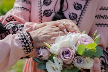 Nikah buketinde alyansları olan yeni evlilerin elleri. Gelinin ve damadın elleri bir buket çiçekte.