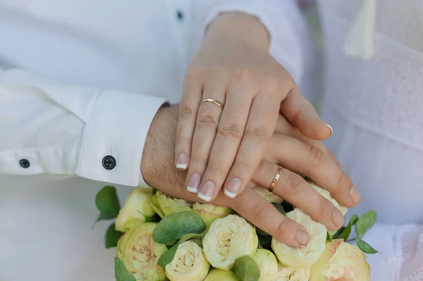 婚礼花束上戴着结婚戒指的新婚夫妇的手 新娘和新郎的手放在一束鲜花上 — 图库照片