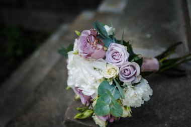 Gelinin buketinde renkli çiçeklerle bir çift altın alyans..