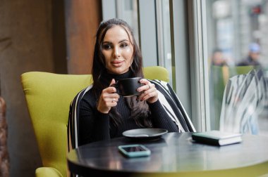Business woman sitting in the office at the window and drinking coffee.