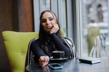 Business woman sitting in the office at the window and drinking coffee.