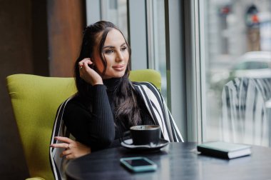 Business woman sitting in the office at the window and drinking coffee.