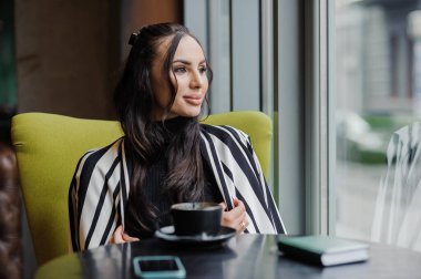 Business woman sitting in the office at the window and drinking coffee.