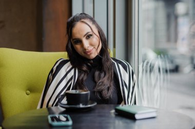 Business woman sitting in the office at the window and drinking coffee.