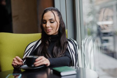 Business woman sitting in the office at the window and drinking coffee.
