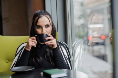 Business woman sitting in the office at the window and drinking coffee.