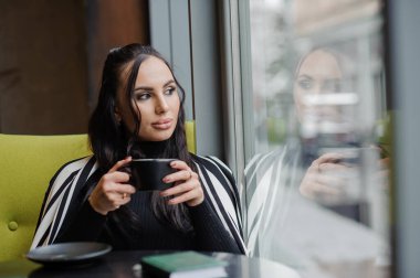 Business woman sitting in the office at the window and drinking coffee.