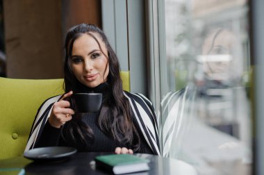 Business woman sitting in the office at the window and drinking coffee.