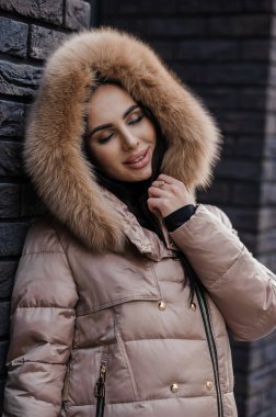 Beautiful young woman outdoors in a brown coat, in the background a brick wall.