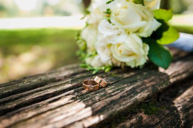 Kahverengi arka planda bir çift altın alyans, arka planda beyaz çiçekli bir buket..