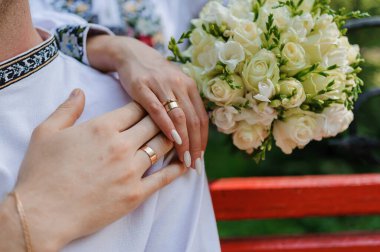 Yeni evlilerin elinde altın alyanslar. Ulusal Ukrayna elbiseli kadın ve erkek. Beyaz çiçekli gelin buketi.