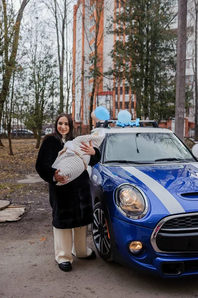 stock image A beautiful woman stands near a car and holds a baby wrapped in a blanket