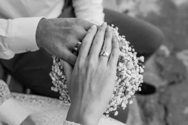 新婚夫婦の手に結婚指輪 背景に花の花束 男と女の手に金の指輪 — ストック写真
