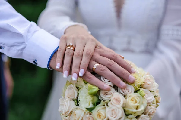 부부의 손에는 반지가 있는데 뒤에는 꽃다발이 있습니다 남녀의 금고리가 — 스톡 사진