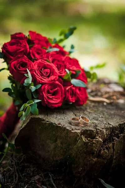 一束金光闪闪的结婚戒指挂在树桩上 背景是一束红玫瑰 — 图库照片