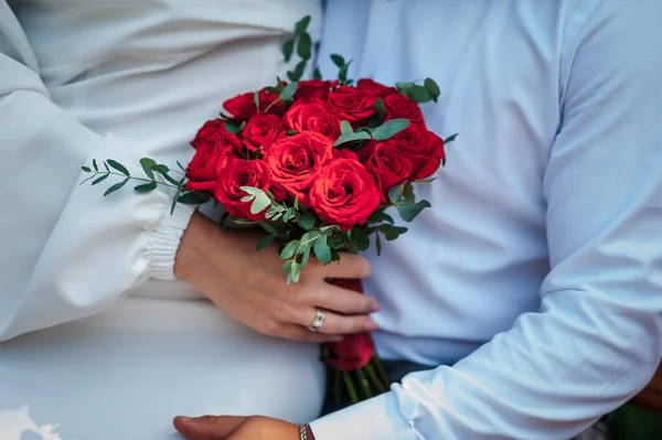 Bouquet of red roses in the hands of the bride. Bride\'s bouquet of red roses in the hands of a woman