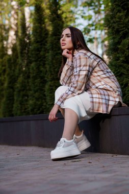 Ekose gömlekli bir kız bankta oturuyor. Güzel bir genç kadının portresi.