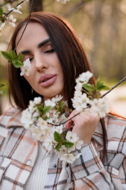 Ekoseli bir kız çiçek açan bir ağacın yanında duruyor. Güzel bir kadının portresi.