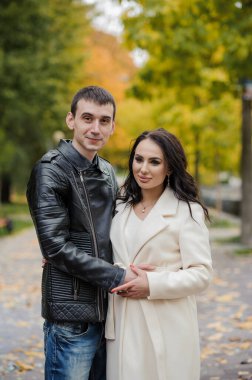 Bir erkek hamile karısına sarılır. Siyah ceketli bir adam beyaz önlüklü bir kadına sarılıp öpüyor. Sonbahar