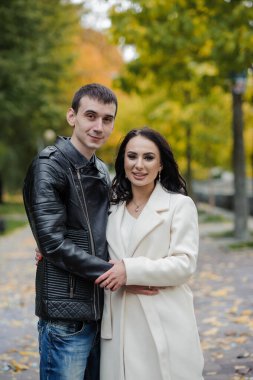 Bir erkek hamile karısına sarılır. Siyah ceketli bir adam beyaz önlüklü bir kadına sarılıp öpüyor. Sonbahar