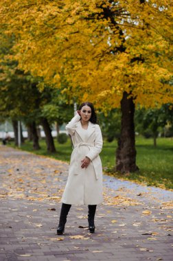 Sonbahar parkında beyaz ceketli esmer kız.