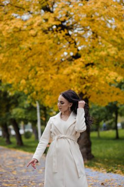 Sonbahar parkında beyaz ceketli esmer kız.