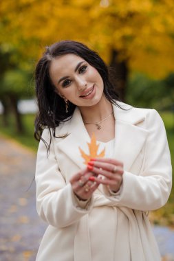 Sonbahar parkında beyaz ceketli esmer kız.