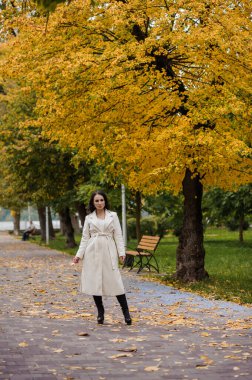 Sonbahar parkında beyaz ceketli esmer kız.