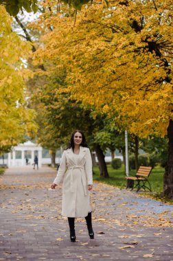 Sonbahar parkında beyaz ceketli esmer kız.