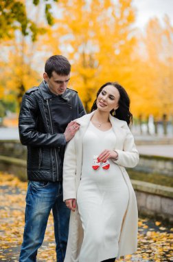 Bir erkek hamile karısına sarılır, bir kadın bebeğinin çoraplarını karnının yanında tutar.