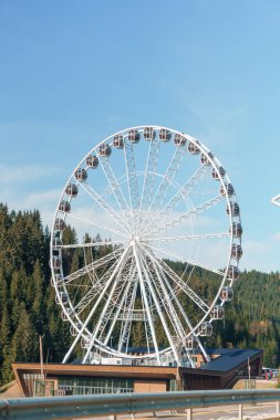 Bukovel 'de mavi gökyüzünün önünde büyük, uzun, beyaz dönme dolap. Karpatlar