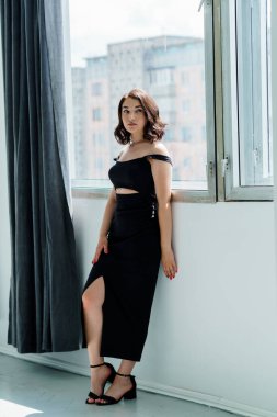 Pencerenin yanında duran siyah elbiseli güzel bir kızın portresi.