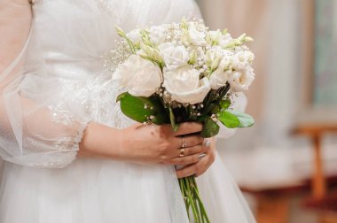 Gelinin elinde güzel bir düğün buketi. Gelinin ellerinde beyaz güller olan buket.
