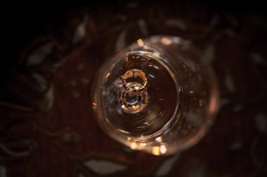 Kahverengi arka planda altın alyanslar. Altın alyanslar bir bardak köpüklü şarapta