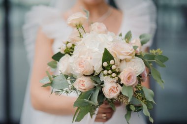 Gelinin elinde güzel bir düğün buketi. Gelinin ellerinde beyaz güller olan bir buket.