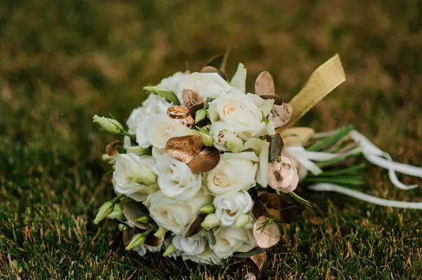 Bir buket beyaz çiçekte bir çift altın alyans. Bir buket gülün üzerinde altın yüzükler