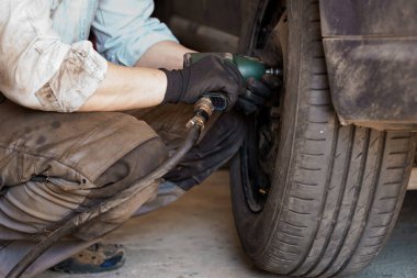 Bir tamirci bir araba şasesini tamir eder. Bir adam tornavida kullanarak araba tekerleklerini çıkartıyor.