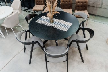 Siyah ahşap masa ve yumuşak kumaş döşemeli siyah tahta sandalyeler. Masada cam vazo var.