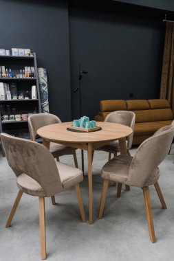 Sarı ahşap masa, bej ahşap koltuklar ve yumuşak kumaş döşeme. Masada mavi porselen bir çaydanlık ve mavi kupalar var.