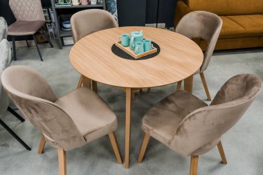 Sarı ahşap masa, bej ahşap koltuklar ve yumuşak kumaş döşeme. Masada mavi porselen bir çaydanlık ve mavi kupalar var.