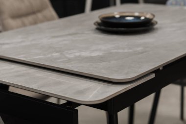 Gri ahşap masa, bej ahşap koltuklar ve yumuşak kumaş döşeme. Masadaki mavi porselen tabaklar.