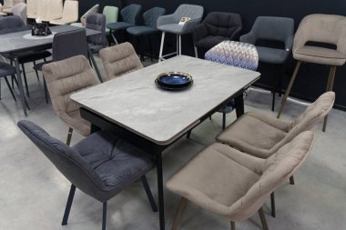 Gri ahşap masa, bej ahşap koltuklar ve yumuşak kumaş döşeme. Masadaki mavi porselen tabaklar.