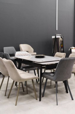 Gri ahşap masa, bej ahşap koltuklar ve yumuşak kumaş döşeme. Masadaki mavi porselen tabaklar.