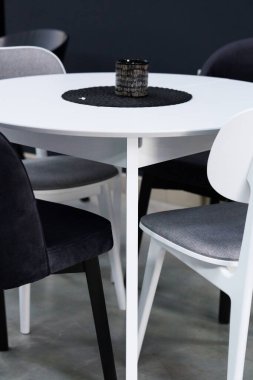 Beyaz ahşap masa, siyah ve beyaz tahta sandalyeler ve yumuşak kumaş döşeme. Masanın üzerinde siyah beyaz bir mum var.