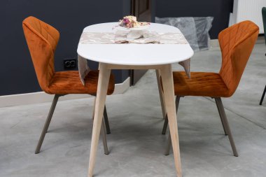 Beyaz ahşap masa, turuncu sandalyeler ve yumuşak kumaş döşeme. Masanın üzerinde çok renkli bir buket çiçek olan beyaz bir teslimat var.