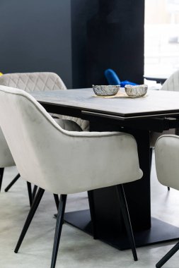 Gri ahşap katlama masası ile gri sandalyeler ve yumuşak kumaş döşeme. Masanın üzerinde siyah bir porselen plaka var.