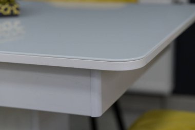 Beyaz masa, yumuşak kumaş döşemeli sarı ahşap sandalyelerle birleştirilmiş. Masada bir çatal bıçak takımı var.