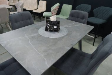 Gri ahşap masa ve yumuşak kumaş döşemesi olan gri ahşap sandalyeler. Masada siyah bir peçete tutacağı var.