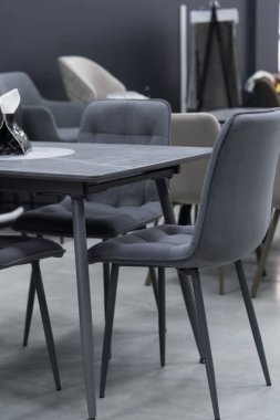 Gri ahşap masa ve yumuşak kumaş döşemesi olan gri ahşap sandalyeler. Masada siyah bir peçete tutacağı var.