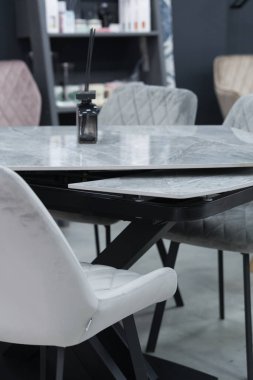 Gri ahşap masa, yumuşak kumaş döşemeli gri ahşap sandalyelerle tamamlanmış. Masanın üzerinde tütsü çubukları olan siyah bir kavanoz.